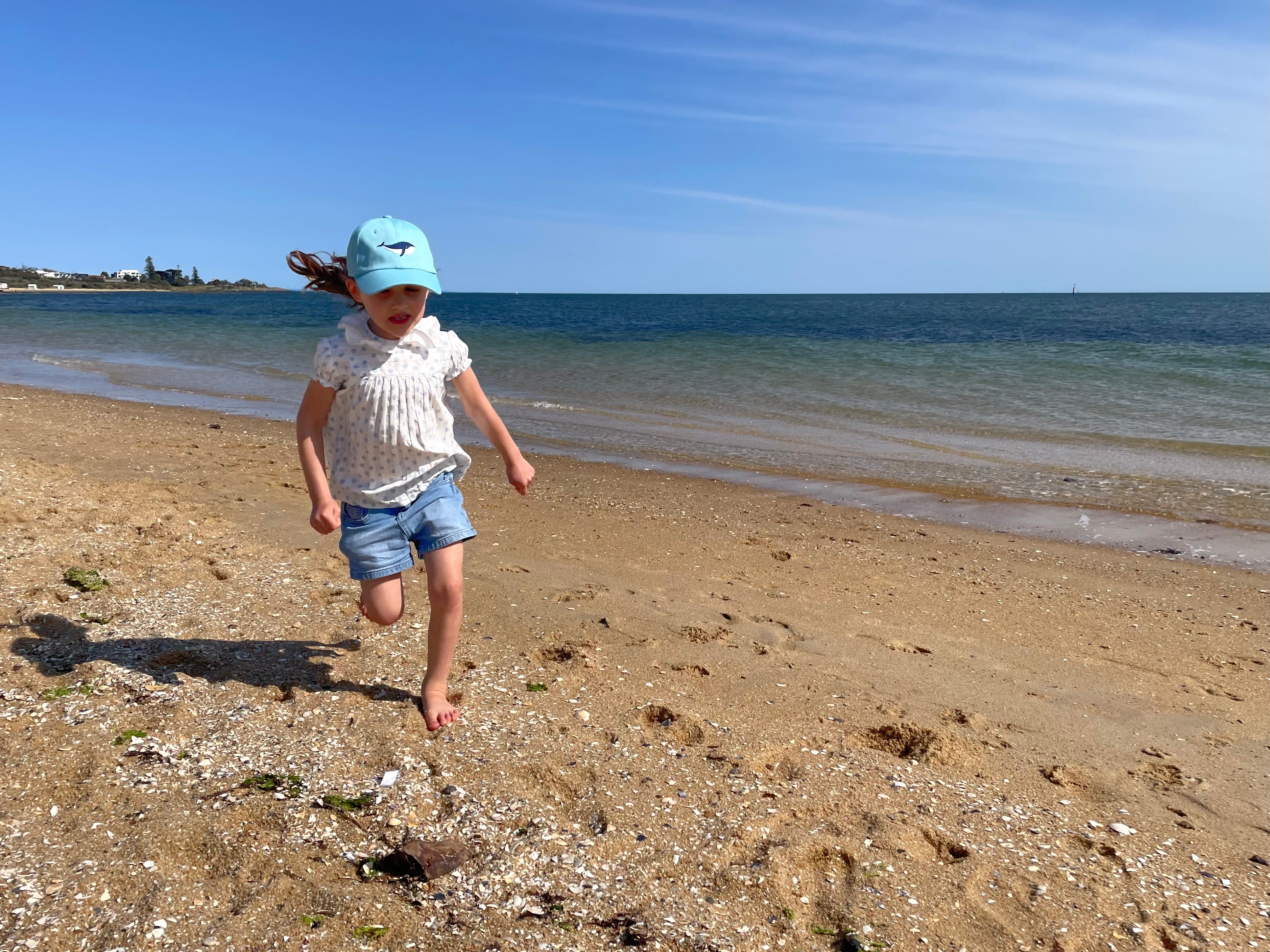 a little girl running on the beach wearing the Whale Cap